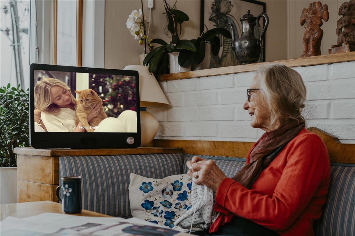 Kvinne strikker meds hun snakker med barnebarn via KOMP-skjerm. Foto. - Klikk for stort bilde